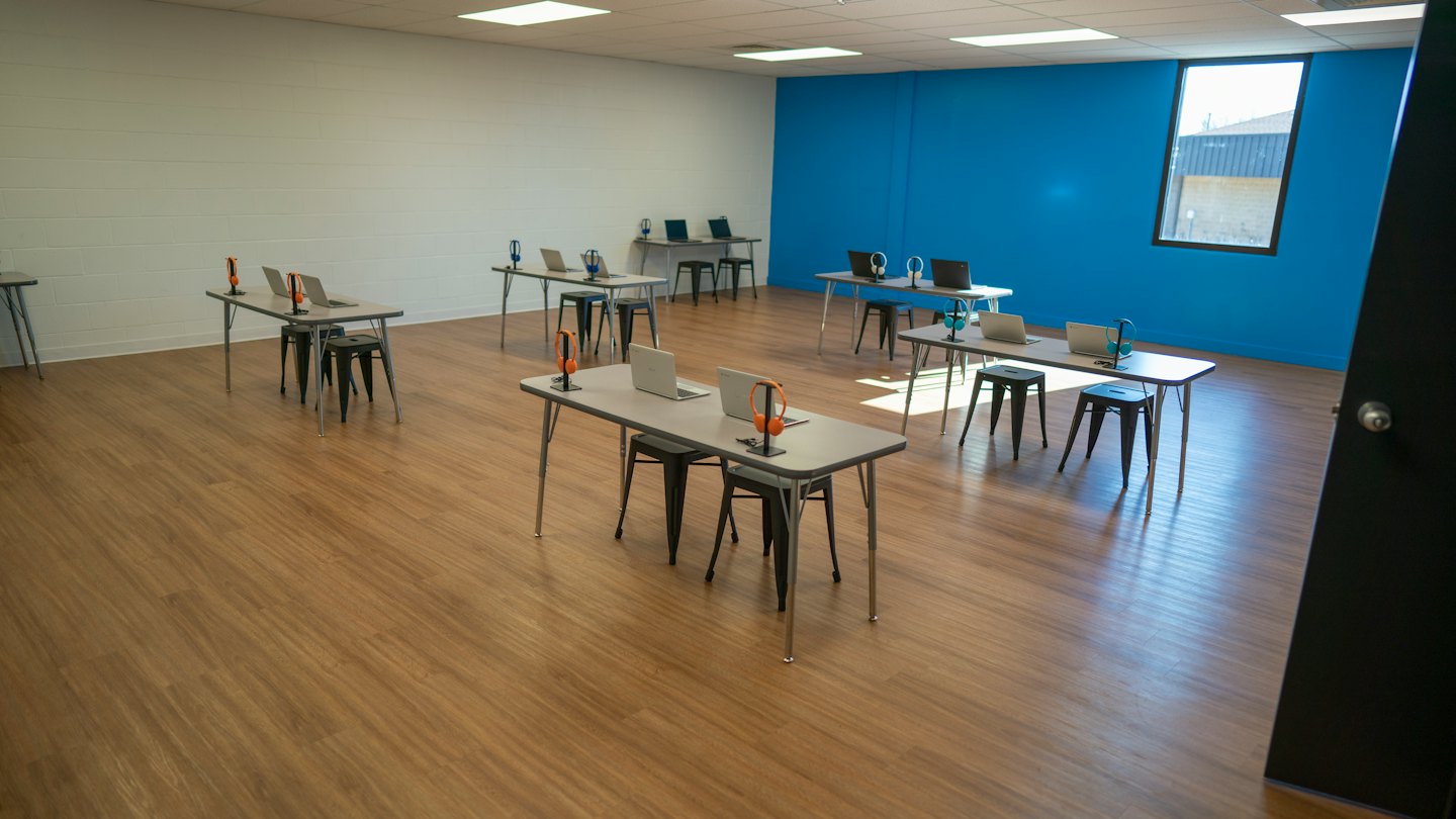 Moderner Schulungsraum mit Laptops und Kopfhörern auf Tischen.